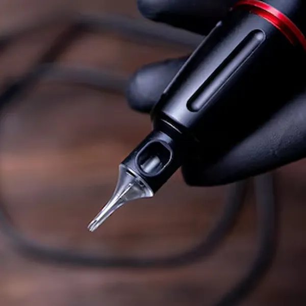 Gray tattoo cartridge inserted in black tattoo machine grip with red accent