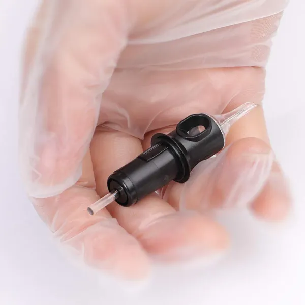 Tattoo cartridge held in gloved hand showing needle tip and grip interface