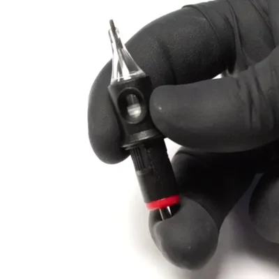 Close-up of REBEL Precision round shader tattoo cartridge held in gloved hand showing exposed needle tip