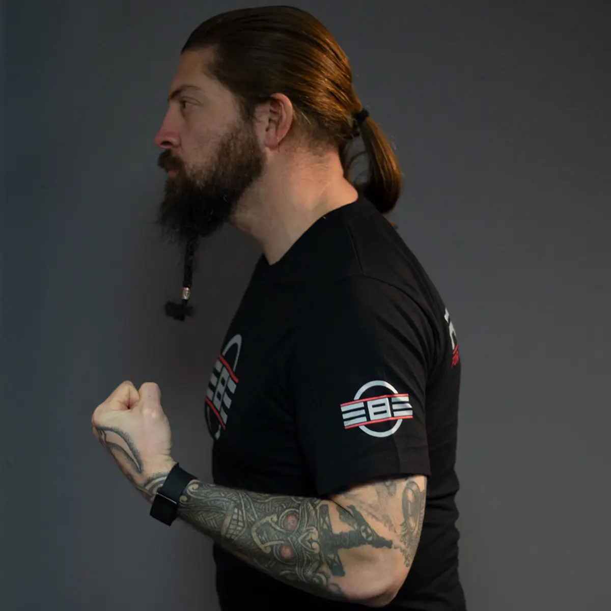 Tattooed male artist wearing REBEL Precision Tee, side profile, REBEL sleeve logo visible, full arm tattoo