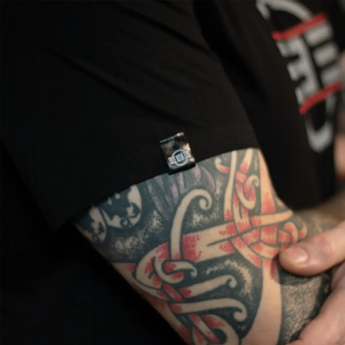 REBEL THREAD silk tab on sleeve seam close-up, full color tattoo sleeve visible on arm