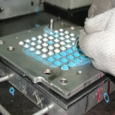 Gloved worker peeling silicone membranes from a multi-cavity steel mold during tattoo cartridge manufacturing
