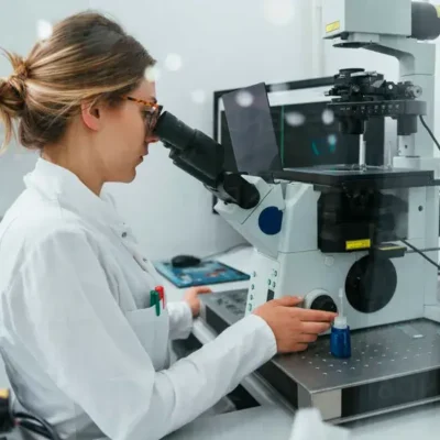 Technician inspecting tattoo needles under a high-resolution microscope for quality control in manufacturing
