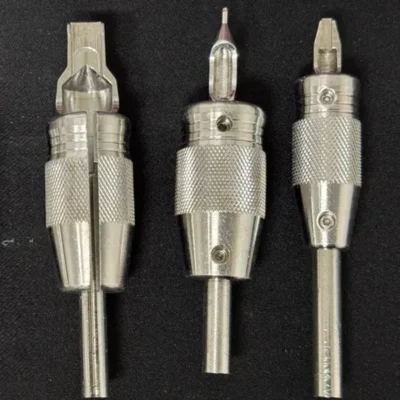 Three vintage steel tattoo tube and grip assemblies — knurled grips with screw locks and varying tip styles on steel needle bars