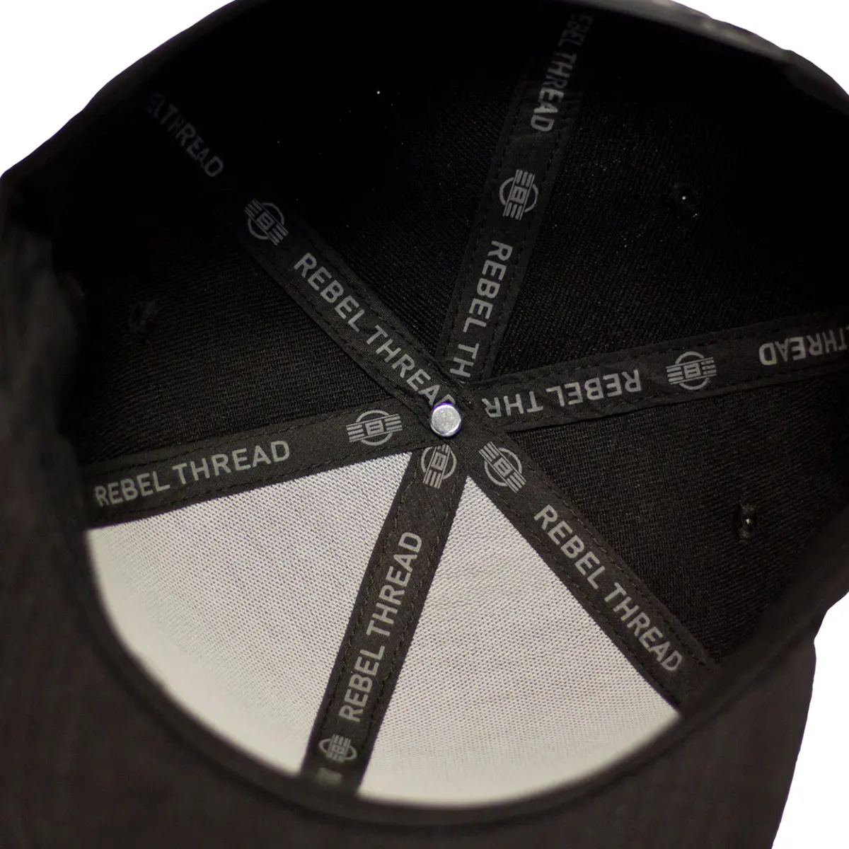 Close-up inside view of the REBEL Snapback Hat showing REBEL Thread printed inner taping across all six panels of the black cotton cap