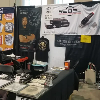REBEL and Killer Silver banners with Caesar poster and tattoo cartridge boxes at a convention booth