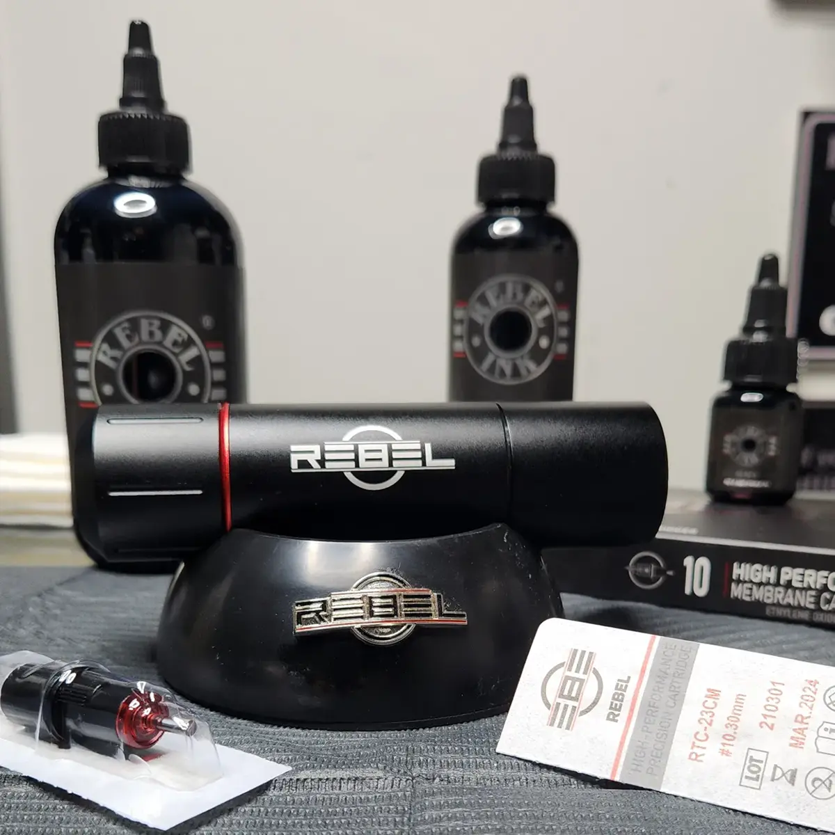 Tattoo machine holder with REBEL Ink bottles, cartridge box, sealed cartridge and REBEL tattoo machine prop